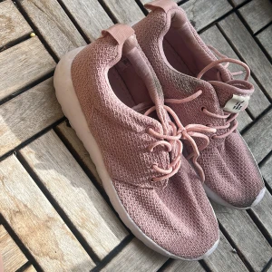 Rosa sneakers med vit sula - Snygga rosa sneakers med stickad ovandel och vit platt sula. Skorna har snörning och en praktisk ögla bak för enkel påtagning. Perfekta för dig som gillar en sportig och trendig look.