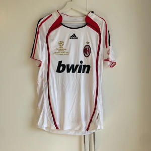 AC Milan Kaka' 22 Champions League tröja - AC Milan fotbollströja från Adidas med Kaka' 22 på ryggen. Officiell Champions League-final 2007 design, vit med röda och svarta detaljer. Stora tryck på bröstet och ryggen, klubbmärke och Adidas-logga. Tillverkad i återvunnen polyester.