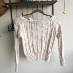 Vit kabelstickad tröja  - Supermysig vit stickad tröja med bred halsringning och långa ärmar. Tröjan har en mönster som ni ser på bilden. Det är stretch i så den är S men passar M oxå. Jag är S och 169cm och den är lite kort på mina armar