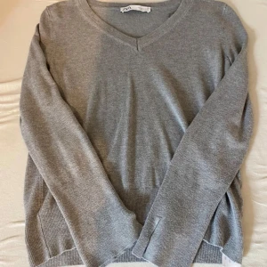 Grå v-ringad tröja från Zara - En stilren grå v-ringad tröja från Zara med lång ärm och ribbade muddar. Knappt använd och är i mycket bra skick 