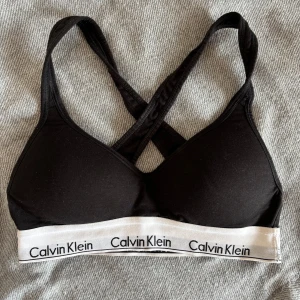 Svart linnetopp Calvin Klein S - Svart linnetopp från Calvin Klein med klassisk vit resår och logga runt om. Snyggt korsade axelband i ryggen och mjuk, stretchig bomullskvalitet. Perfekt för en sportig och chill look. Använd ett fåtal gånger! Nypris: 500kr
