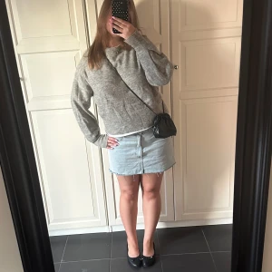 Grå stickad tröja med rund hals - Mysig grå stickad tröja med rund hals och långa ärmar. Tröjan har en relaxed fit och ribbade muddar vid ärmslut och nederkant. Perfekt att slänga på sig när det är kyligt ute.