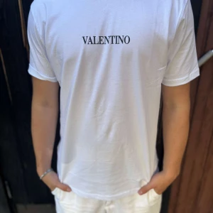 Vit t-shirt från Valentino - Snygg vit t-shirt från Valentino med klassisk rund hals och svart logotyptryck på bröstet. T-shirten är i mjuk bomull och har korta ärmar. Perfekt för en clean och stilren look.