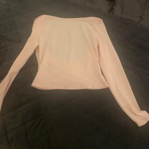 Ljusrosa långärmad topp med öppen rygg - Supersöt ljusrosa långärmad topp med croppad passform och stor öppen rygg. Tunn och mjuk, perfekt att styla med höga jeans eller kjol. Enkel men ändå riktigt snygg detalj med den öppna ryggen som gör att du sticker ut.