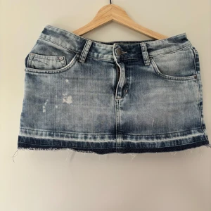 Blå jeanskjol med fransig kant - Snygg blå jeanskjol med slitna detaljer och fransig, rå kant nertill. 