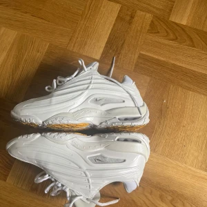 Nike Nocta Step 2 Drake - Nike Nocta Step 2 Drake sneakers i helvitt med detaljer i mesh och syntet. Snygg futuristisk design med silverfärgad mini-swoosh på sidan och gula detaljer under sulan. Skorna har snörning och en chunky vibe som sticker ut.