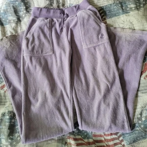 Ljuslila mjukisbyxor Juicy Couture XS - Supermjuka ljuslila mjukisbyxor från Juicy Couture i frotté med bred resår och snörning i midjan. Stora fickor fram, bakficka med knapp och broderad JC-logga. Perfekta för chill eller streetstyle.