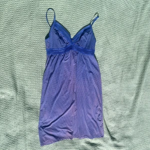 Lila/blå prickig kortklänning från Tchibo - Blå kortklänning från Tchibo med tunna axelband och små vita prickar. Klänningen har spetsdetaljer och är väldigt luftig.  Fläckig i färgen så säljer därför för billigt pris. 