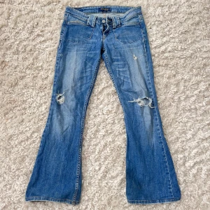 Levis 517 bootcut jeans blå - Snygga blå Levis 517 lågmidjade jeans med bootcut och slitna detaljer på benen. Klassisk femficksmodell med låg midja och utställda ben. Innerbenslängd : 75cm, Midjemått : 39cm
