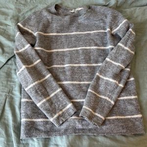 Grå randig stickad tröja H&M - Mysig grå stickad tröja från H&M med vita horisontella ränder. Tröjan har rund halsringning, långa ärmar och ribbade muddar. Perfekt för lager-på-lager och chill dagar.