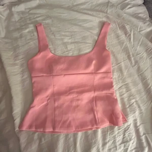 Rosa linnetopp med rosett och cut out - Supersöt ljusrosa linnetopp med breda axelband och figurnära passform. Toppen har en stor rosett och cut out-detalj i ryggen som gör den extra unik. Perfekt för dig som vill sticka ut med en feminin och trendig look!🩷💘