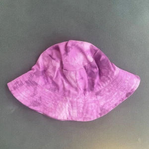 Lila bucket hat Rusta - Snygg lila bucket hat i 100% bomull med batikmönster. Perfekt för att lyfta din stil med en cool och avslappnad vibe. Hatten har bred brätte och är lätt att matcha med olika outfits.