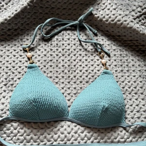 Turkos bikini med pärldetalj - Supersnygg turkos bikiniöverdel med ribbad struktur och guldfärgade detaljer med pärla på axelbanden. Triangelformade kupor och knyt i nacken och ryggen. Tillverkad i stretchig polyesterblandning som sitter skönt på kroppen. Köpt på SHEIN i stl S. Bara att höra av dig!🥰