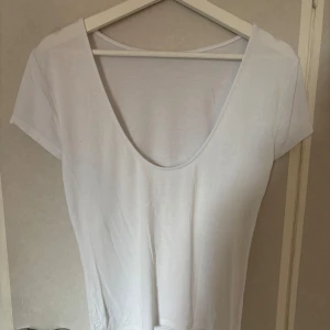 Vit t-shirt med djup urringning - Enkel och stilren vit t-shirt med korta ärmar och djup rund urringning framtill. T-shirten är i mjukt och tunt bomullstyg, perfekt för varma dagar eller som basplagg. Passformen är normal och modellen är klassisk utan tryck eller mönster. Vet ej vart jag köpt den men den är i stl M. Bara att höra av dig!🥰