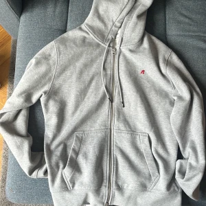 Grå hoodie med dragkedja från Replay - Snygg ljusgrå hoodie från Replay med hel dragkedja, huva med snörning och två stora fickor framtill. Mjuk insida och liten röd Replay-logga på bröstet. Perfekt för chill dagar eller när du vill ha en clean och enkel look. Storlek L nypris 1200