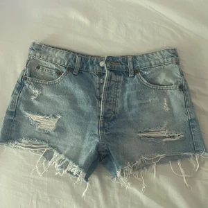 Ljusblå jeansshorts från Zara - Snygga ljusblå jeansshorts från Zara med medelhög midja, slitna detaljer och fransig kant. Klassisk femficksmodell med knappgylf och bälteshällor. Perfekta för sommaren och ger en avslappnad vibe. Något liten i storleken