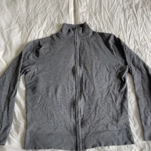 Grå kofta från Tommy Hilfiger M (Passar S) - Stilren och klassisk grå sweatshirt från Tommy Hilfiger med rund halsringning (crewneck). Tröjan har ett diskret, broderat Tommy Hilfiger-märke på vänstra bröstet – perfekt för dig som gillar enkel och tidlös design med hög kvalitet.  👕 Färg: Grå 📏 Storlek: M 🧵 Material: Mjuk och bekväm bomullsblandning 🎯 Passform: Normal 📦 Skick: Mycket fint skick – inga fläckar, hål eller noppor  En mångsidig tröja som passar lika bra till jeans som till mjukisbyxor. Perfekt för vardagen!