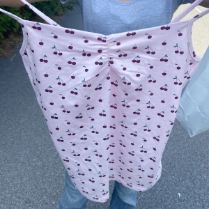 Rosa linnetopp med körsbärsmönster - Supersöt rosa linnetopp med tunna axelband och gulligt körsbärsmönster över hela toppen. Lätt rynkning framtill ger en extra fin detalj. Perfekt för varma dagar och enkel att matcha med jeans eller kjol. Storlek L men passar bra på mos som är xxs/xs då det är väldigt tajt. 