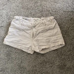 Randiga shorts från Massimo Dutti - Snygga, ljusa shorts från Massimo Dutti med tunna vertikala ränder i vitt och beige. Low waste. Klassisk design med knapp och dragkedja framtill samt fickor både fram och bak. Perfekta för varma sommardagar och riktigt sköna att ha på sig.