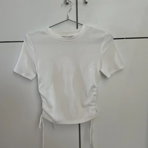 Vit ribbad topp med snörning från Zara - Vit ribbad topp från Zara med korta ärmar och rund hals. Snörningsdetalj i sidorna som gör att du kan justera längden och får toppen mer croppad. Skulle säga att den passar xs bättre än S. Lappen kvar o aldrig använd 🌸