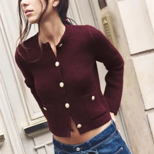 Vinröd kofta med guldknappar - Vinröd kofta med snygga guldknappar framtill och två fickor. Modellen är croppad och har lång ärm. Perfekt för dig som vill ha en klassisk men trendig look. Stickad i mjukt material och passar till både jeans och kjol.