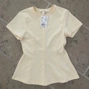 Ljusgul figursydd topp från H&M - Supersnygg gul topp från H&M med figursydd passform och korta ärmar. Tröjan har bara testats en gång men har några sminkfläckar som borde gå bort efter en tvätt💗