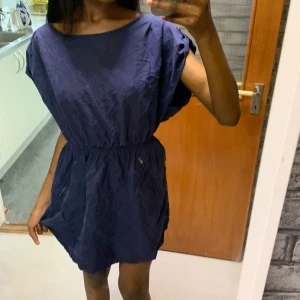 Mörkblå kortklänning med dragkedja - Snygg mörkblå kortklänning med resår i midjan och dragkedja bak. Klänningen har lös passform, korta ärmar och praktiska fickor med dragkedja framtill. Perfekt för dig som gillar enkel men stilren design. Vet dock inte vart den är ifrån samt storleken, men skulle gissa är den är i storlek S/M lite stor för mig 
