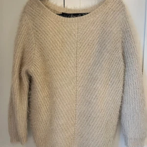 Beige fluffig stickad tröja - Mysig beige stickad tröja med fluffig känsla och avslappnad passform. Tröjan har rund halsringning och långa ärmar, perfekt för lager på lager under kyliga dagar. Enkel att styla till jeans eller kjol för en chill look.