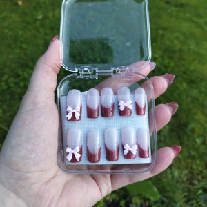 Vinröda lösnaglar med rosetter - Säljer ett set med handgjorda lösnaglar i en snygg  nude design. Fyra av naglarna har söta ljusrosa 3D-rosetter. Storleken är s/m med måtten: 15, 11, 12, 11, 9 (mm). Lim ingår ej😊