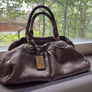 Brun skinnväska Marc by Marc Jacobs - Säljer en brun handväska från Marc by Marc Jacobs i äkta skinn med snygga guldfärgade metalldetaljer och dubbla handtag i stora modellen!