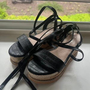 Svarta platåsandaler med snörning - Snygga svarta sandaler med platåsula, Remmar i croco-mönstrad syntet och långa snören att knyta runt vristen🤍De är nästa oanvända och utan några defekter😊