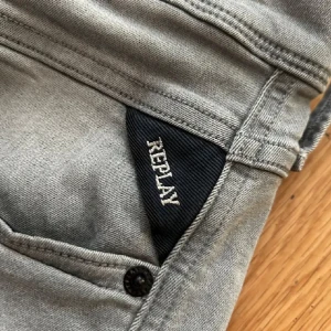 Gråa anbass Replay jeans, W28 L32 - Snygga grå jeans från Replay med klassisk femficksdesign och svarta detaljer vid fickan. Jeansen har en rak passform och är tillverkade i mjukt denimtyg.