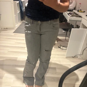 Grå jeans med slitningar från Gina Tricot - Snygga grå jeans från Gina Tricot i storlek 158. Modellen har raka ben med lätt bootcut och slitna detaljer på knäna för en cool look. Klassisk femficksdesign och normal passform. Perfekta till sneakers eller boots.