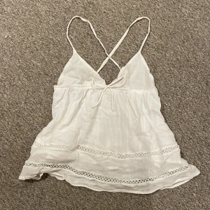 Vit linnetopp från Gina Tricot - Supersöt vit linnetopp från Gina Tricot med tunna korsade axelband och knyt fram. Toppen har volangig nederdel och fina spetsdetaljer längst ner. Bara använd ett fåtal gånger. 