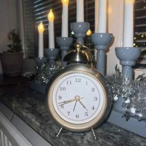 Klassisk silverfärgad väckarklocka - Retroinspirerad väckarklocka i silverfärgat metall med rund form och vita urtavla. Klockan har tydliga svarta siffror, två ben och en guldfärgad ring upptill. Perfekt som snygg inredningsdetalj på nattduksbordet eller skrivbordet.