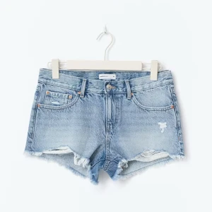 Ljusblå jeansshorts med fransar - Snygga ljusblå jeansshorts med fransiga kanter och slitna detaljer. Klassisk femficksmodell med knapp och dragkedja. Perfekta för varma dagar och en avslappnad stil. 
