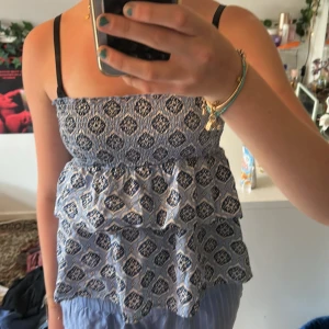 Blå mönstrad linnetopp Gina Tricot - Supersöt blå och vit linnetopp från Gina Tricot med smock upptill och volangig nederdel. Toppen har ett snyggt grafiskt mönster och tunna axelband. Perfekt för varma dagar och enkel att styla med jeans eller kjol.