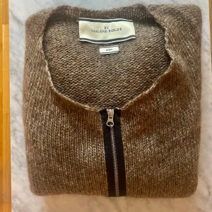 By Malene Birger Brun Stickad Kofta Oversized - Mysig brun stickad kofta från By Malene Birger, märkt som storlek XS men modellen är väldigt oversized så skulle säga att det mer är en M men som passar ändå upp till L. Koftan har en grovstickad känsla, lång ärm och dragkedja framtill. Unik modell som va svår att få tag på, ingick By Malene Birger ”Darlings”. Jättebra skick. 