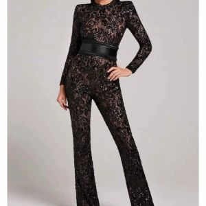 Nadine merabi Svart paljett jumpsuit med bälte - Säljer en svart jumpsuit med långa ärmar, täckt av glittriga paljetter och spetsdetaljer. Den har markerade axlar och ett brett svart bälte i midjan som ger en snygg siluett. Den är uppsydd i benen inifrån (så man kan sprätta upp till den orginala benlängden) benen just nu passar mig som är 158 cm med ett par klackar 