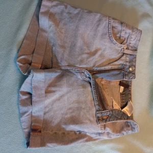 Blå jeansshorts från H&M - Snygga blå jeansshorts från H&M med klassisk femficksdesign, uppvikta benslut och dragkedja framtill. Perfekta för varma dagar och enkla att matcha med allt