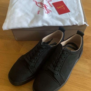 Svarta sneakers från Christian Louboutin - Snygga svarta sneakers från Christian Louboutin i mocka med klassisk röd sula och diskret logga på insidan. Skorna har rund tå, snörning och platt sula. Använda 1 gång. Perfekta för dig som vill ha en stilren och lyxig look med en ikonisk touch. 