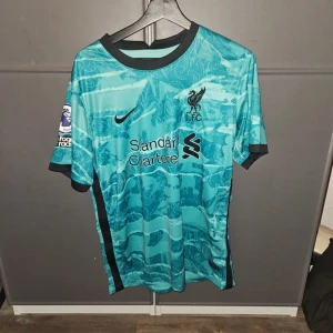 Liverpool Firmino bortatröja Nike 20/21 - Liverpool FC bortatröja med Firmino 9 på ryggen. Turkosblått mönster, svarta detaljer och Premier League-patch på ärmen. Dri-FIT-material som andas, klassisk passform och snygg svart krage. Perfekt för dig som älskar fotboll och vill sticka ut.