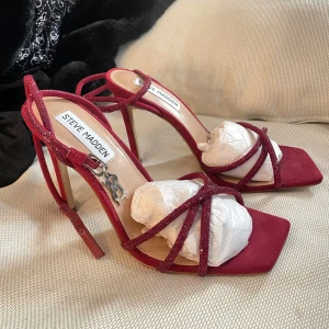 Röda Steve Madden sandaler  - Snygga röda sandaler från Steve Madden med höga klackar och smala glittriga remmar (ca 10cm). Detta är dom snyggaste klackarna jag äger, säljer pga att dom är för smala för min fot🥹. Dom har ett lätt avtryck från sulan då jag försökt gå in dom inomhus, men har helt enkelt kommit till insikt att dom är för små för mig.🥲 aldrig använda utomhus.