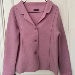 Rosa ulljacka från Georg Maier - Snygg rosa jacka från Georg Maier i mjuk ull. Klassisk kavajmodell med krage, tre knappar framtill och lång ärm. Perfekt för dig som vill ha en stilren och färgglad look. Jackan har en rak passform och är superenkel att matcha. Nytt skick, endast testad! 