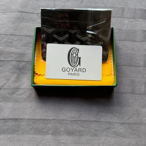 Svart  plånbok med mönster - Säljer en stilren svart plånbok  med ikoniska grafiska mönster i vitt och grått. Plånboken är tunn och smidig, perfekt för kort och sedlar. Kommer i originalask. Riktigt snygg accessoar för dig som gillar lyxiga detaljer.