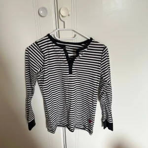 Randig långärmad tröja med snörning - Svartvit randig långärmad tröja från Polarn O. Pyret med snörning vid halsen och svarta muddar. Perfekt för dig som gillar klassisk stil med en twist. Skön bomullskvalitet och passar året runt.