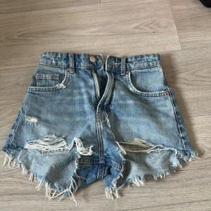 Blå jeansshorts med slitningar från Zara - Snygga blå jeansshorts från Zara med hög midja och fransiga kanter. Shortsen har slitna detaljer framtill. Köparen står för frakten