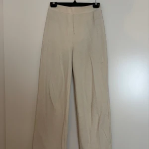 Beiga vida byxor från Zara - Snygga beiga byxor från Zara i storlek S. Byxorna har en rak och vid passform med hög midja och är tillverkade i ett mjukt bomullsmaterial med diskret struktur. Perfekta för en clean och stilren look.
