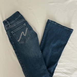 Blå bootcut jeans med broderade fickor - Snygga blå jeans med bootcut passform och coola broderade detaljer på bakfickorna. Jeansen har klassisk femficksdesign, vita kontrastsömmar och är tillverkade i mjukt denimtyg. I princip aldrig använda och är i perfekt skick.