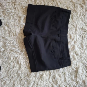 Svarta shorts i bomull med fickor - Snygga svarta shorts i bomull med klassisk design och flera fickor både fram och bak. De har en midwaist passform och stängs med knapp och dragkedja. Perfekta för sommardagar och enkla att matcha med allt. Stilrena och bekväma för en avslappnad look.